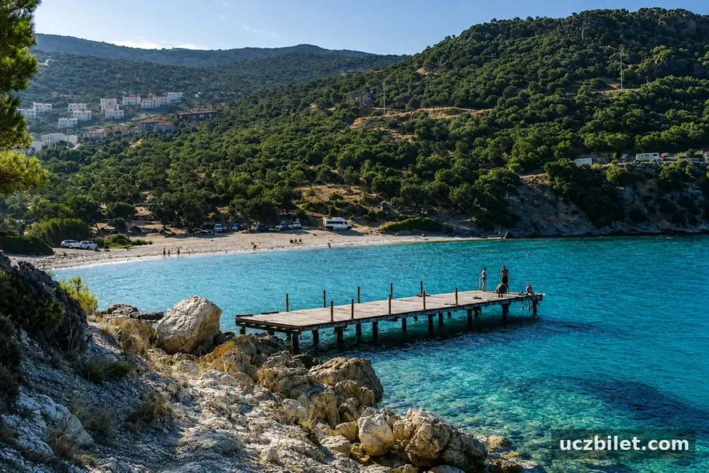 Dikili'deki Hayıtlı Koyu'nun masmavi, berrak sularında uzanan ahşap iskelenin üzerinde duran insanlar, koyun kıyısındaki kumlu plajda güneşlenen ve yüzünen ziyaretçilerle birlikte yemyeşil tepelerin eteklerindeki beyaz evlerin oluşturduğu huzurlu manzarayı tamamlıyor.