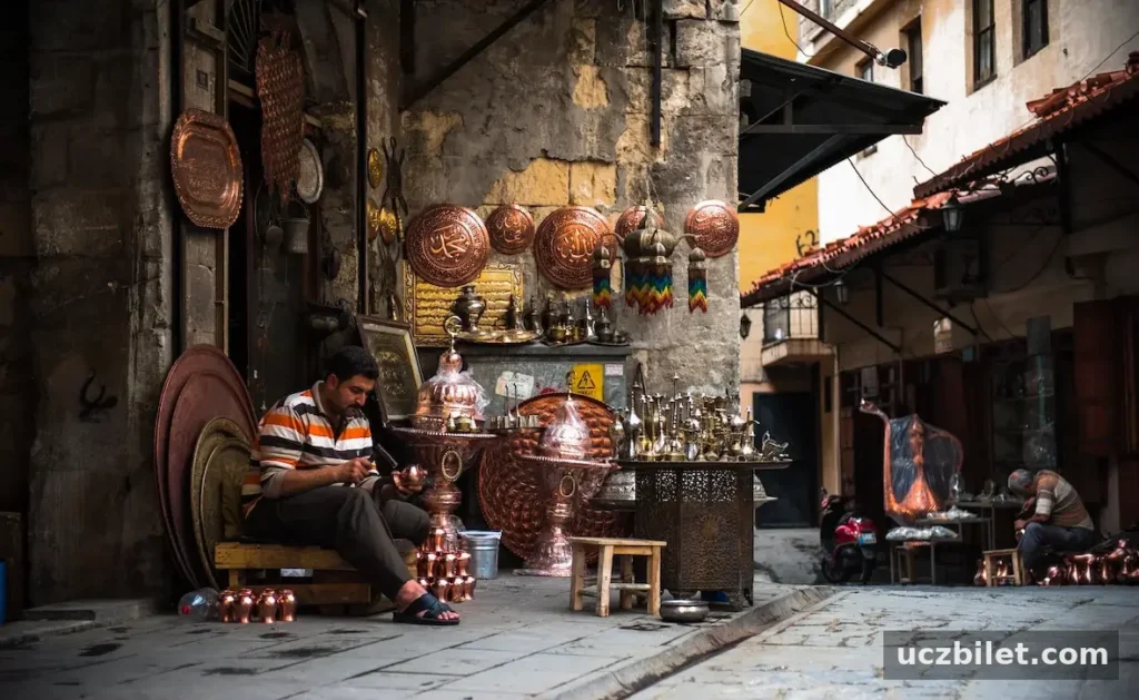 Gaziantep'in tarih kokan dar sokaklarındaki Bakırcılar Çarşısı'nda, el yapımı sayısız bakır ürünün sergilendiği bir dükkanın önünde oturan bir usta, hünerli elleriyle küçük bir bakır objeyi titizlikle işlerken, geleneksel zanaatın canlılığını gözler önüne seriyor.